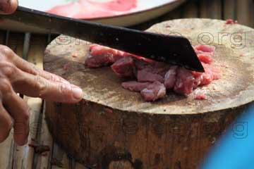 Bei einem Schlachtfest vom Rind beim Thailand Urlaub wird hier auf dem Bild Fleisch auf einer Holzscheibe von einem Baum zerkleinert.
